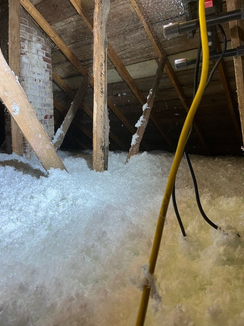 Completed attic insulation with fresh fiberglass blown in around framing and brick chimney
